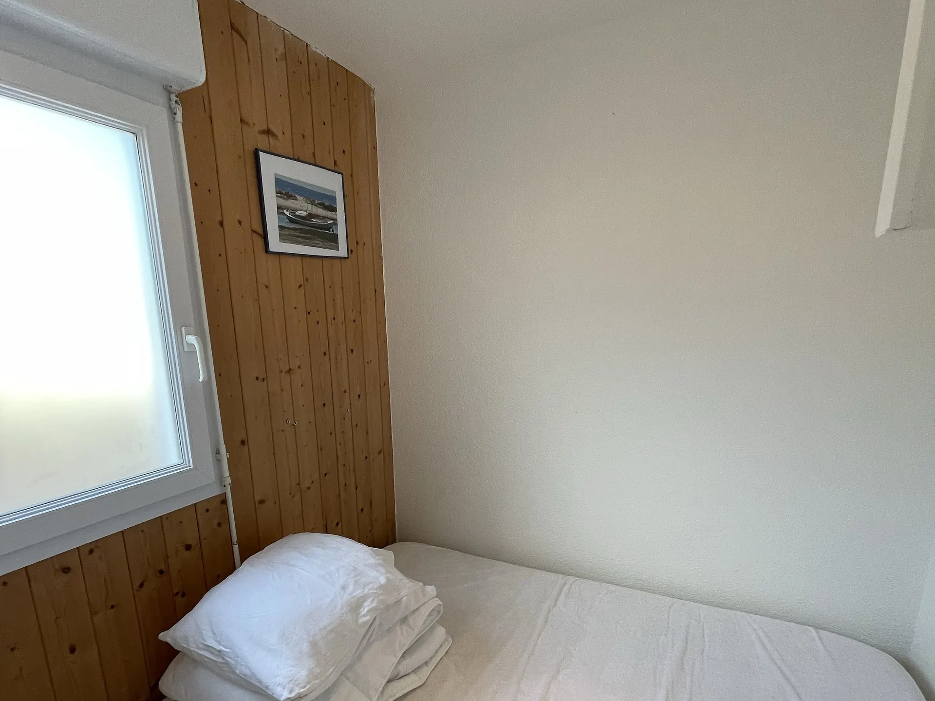 Petite chambre au lit simple, sous son cadre de bateau ; le linge de lit est fourni