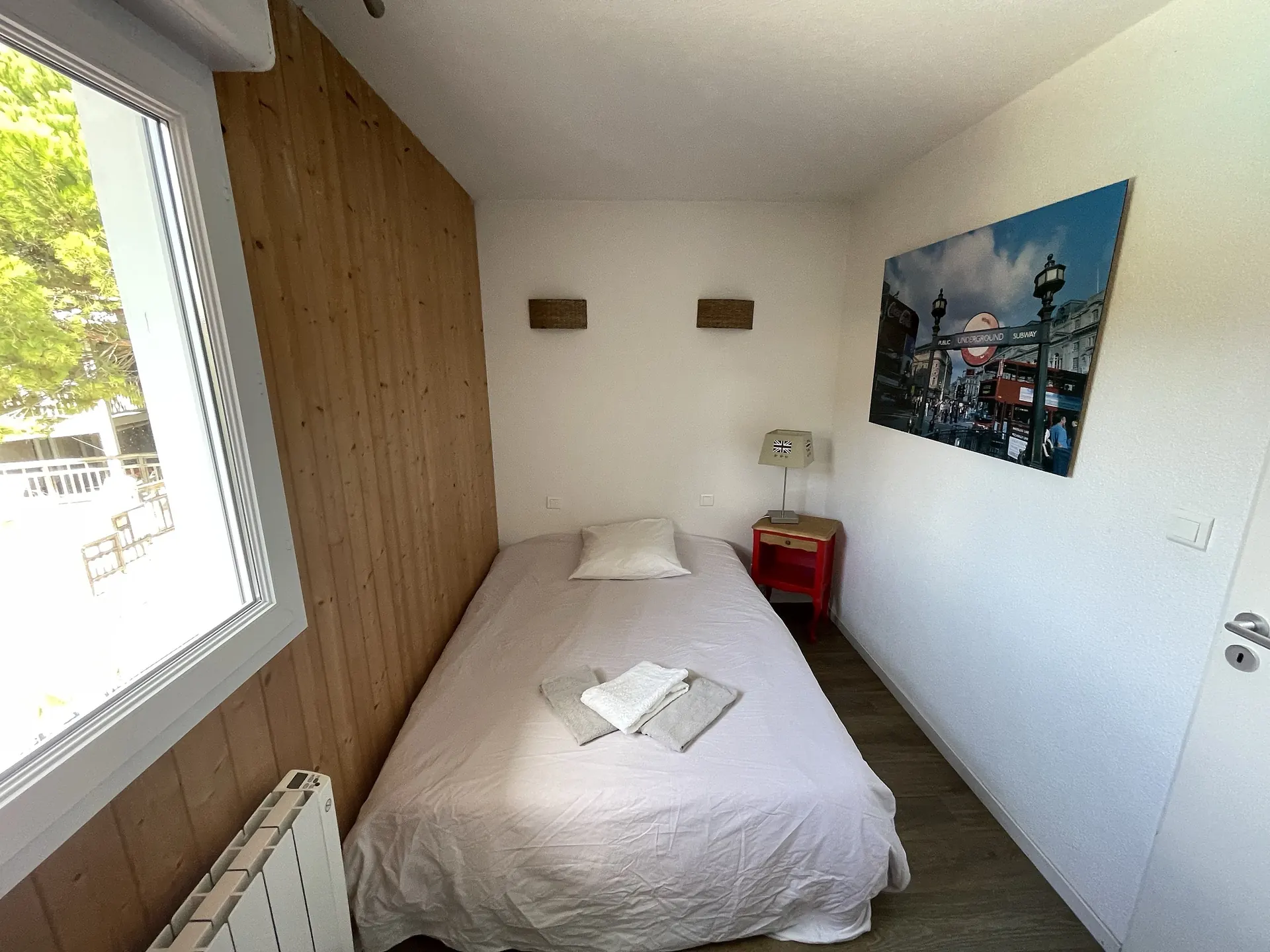 Chambre au lit simple, sa table de chevet rouge et ses appliques en osier
