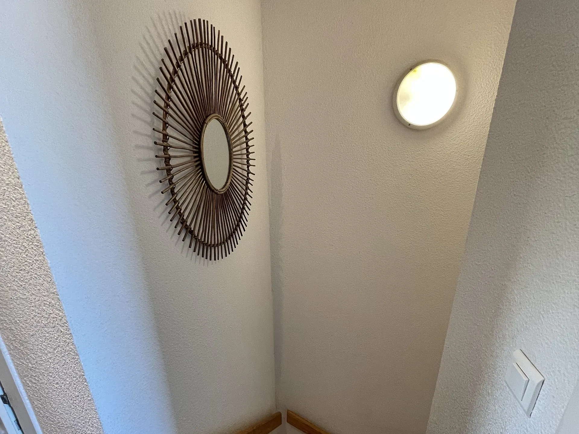 L’escalier de bois qui monte à l’étage, sous son miroir en rotin