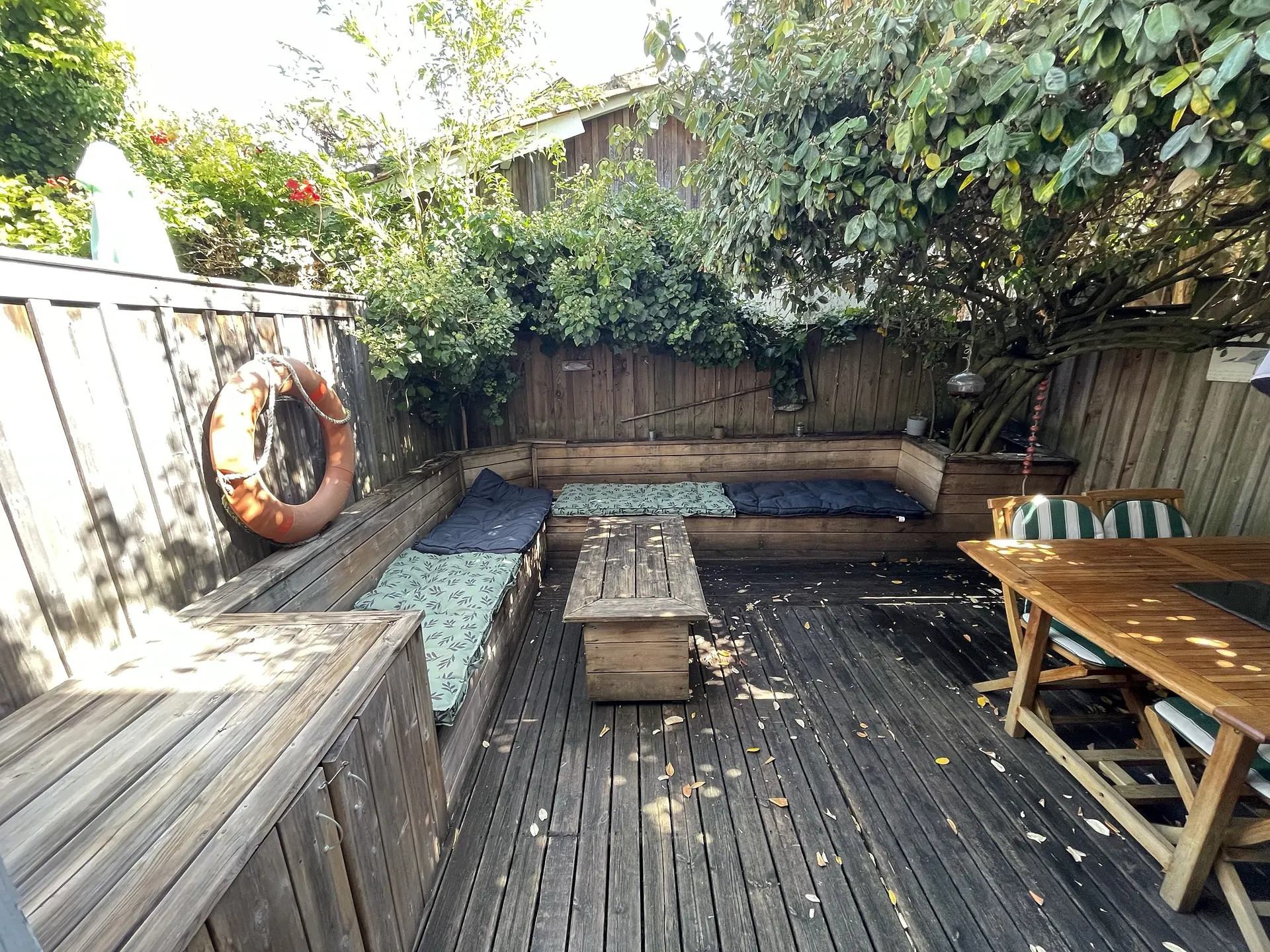 La terrasse en plein soleil, fermée par sa palissade de bois et sa végétation
