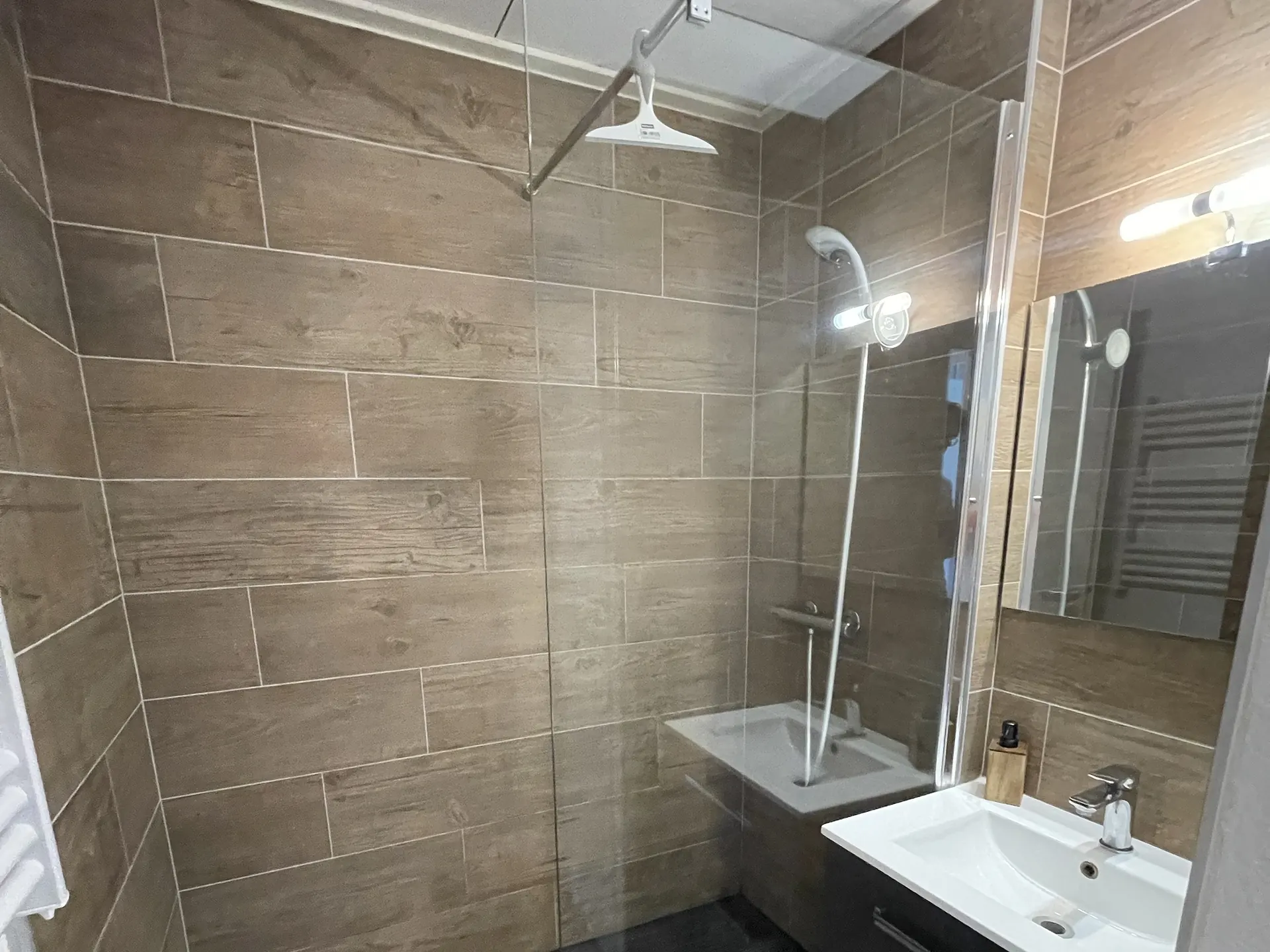 La salle de bains, carrelage imitation bois, douche à l’italienne avec banc et meuble vasque