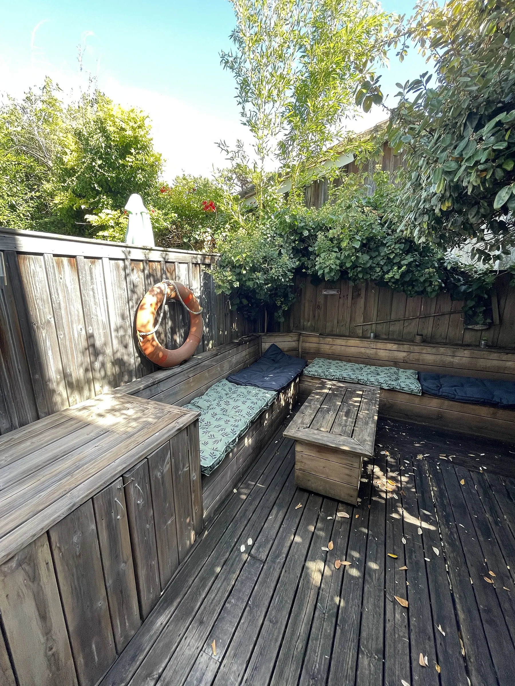 La terrasse en bois privative, ses banquettes à coussins et sa bouée accrochée à la palissade